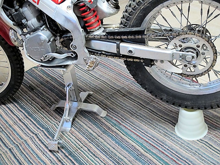 For rear suspension service, the bike must be supported from under the engine, frame or sub-frame; the swingarm cannot bear weight. It will, however, need to be supported to relieve extension pressure on the shock and linkage, thereby allowing their removal. Ugly old rugs come in handy when playing mechanic in the kitchen.